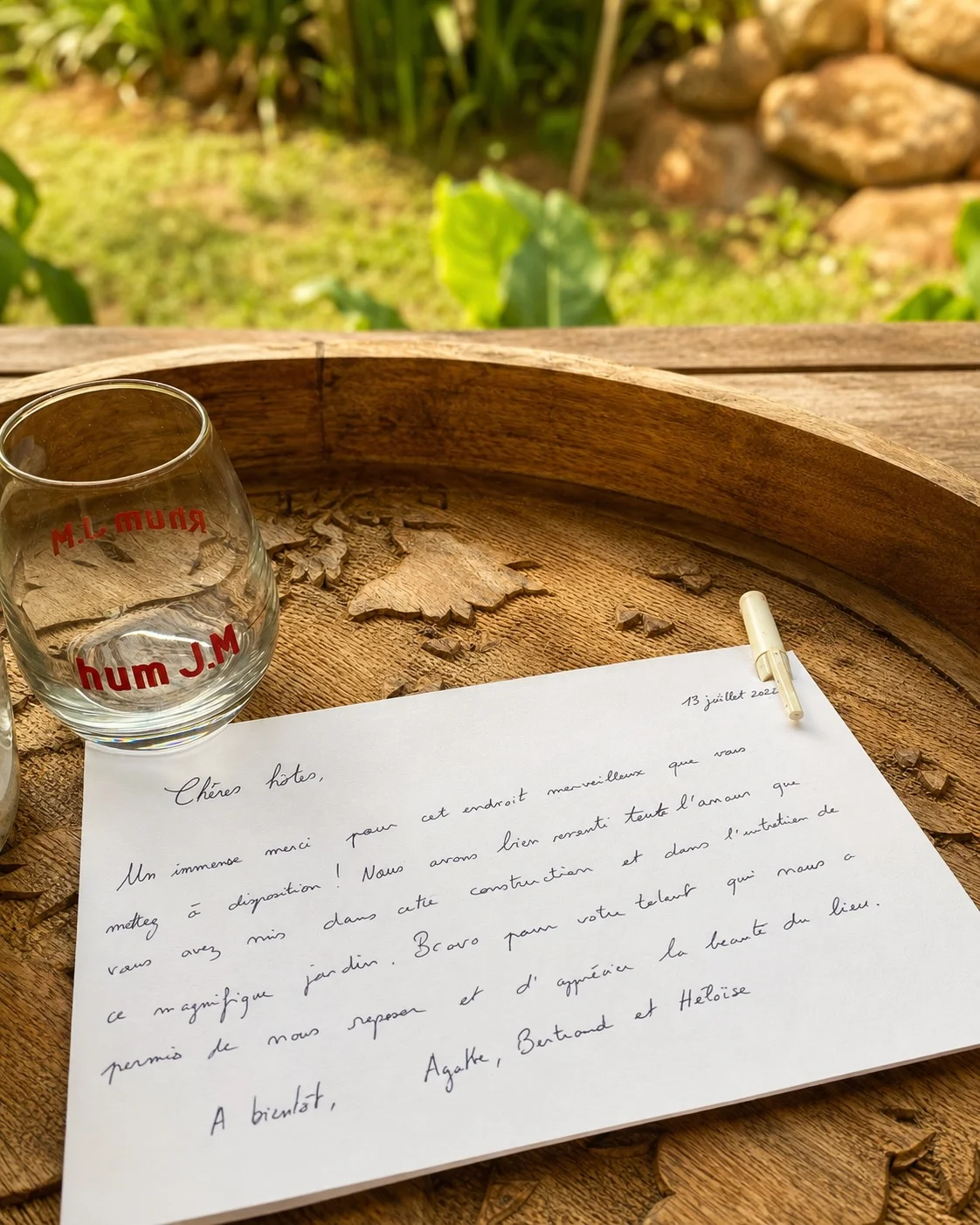 A handwritten note on a carved wooden tray, next to an empty rum glass, garden in the background