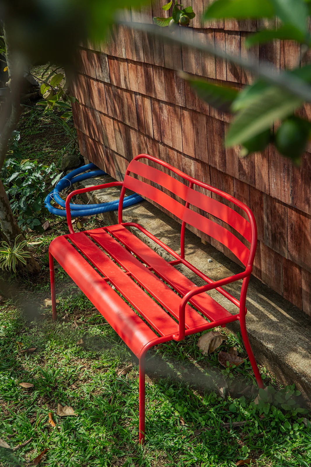 Banc en métal rouge contre le bardage gris en Wapa, Les Vendredis